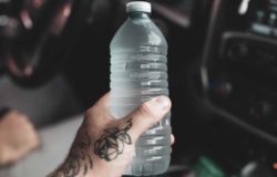 A tattooed hand holds a plastic water bottle.