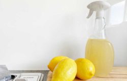 Three lemons placed next to a spray bottle of detergent on a kitchen counter.